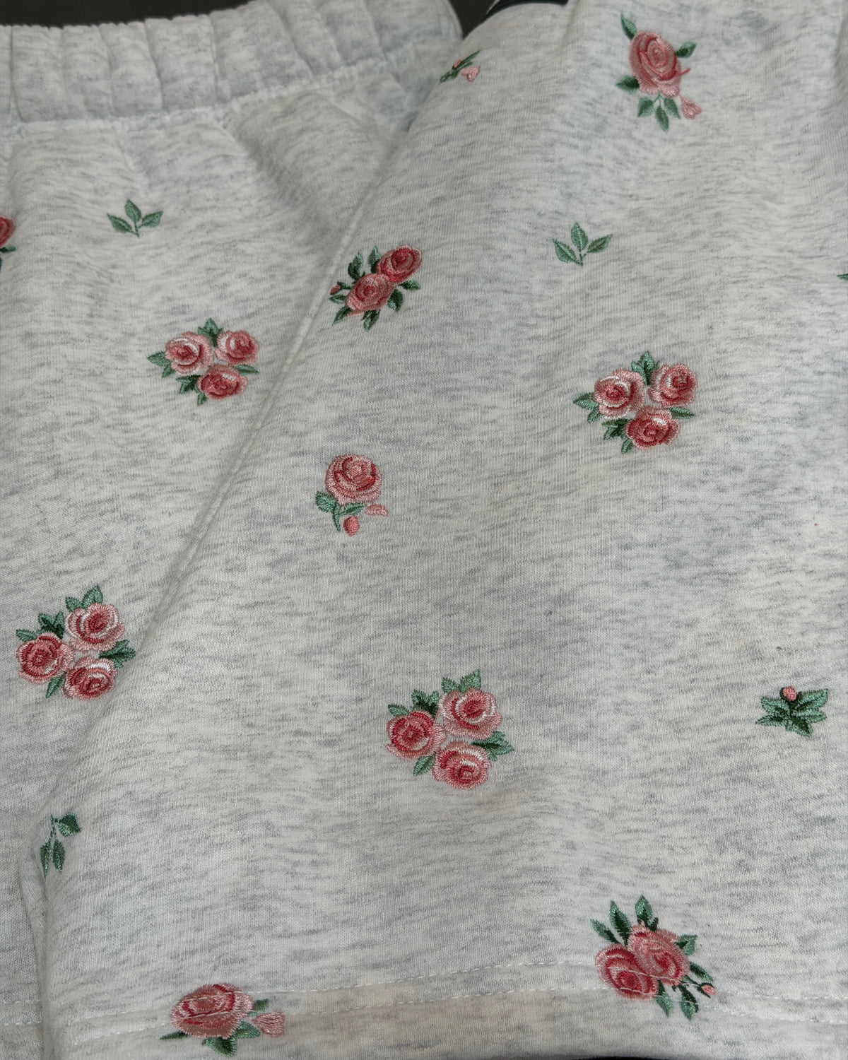 Close-up of light heather gray fabric with a scattered floral print featuring pink roses and green leaves.