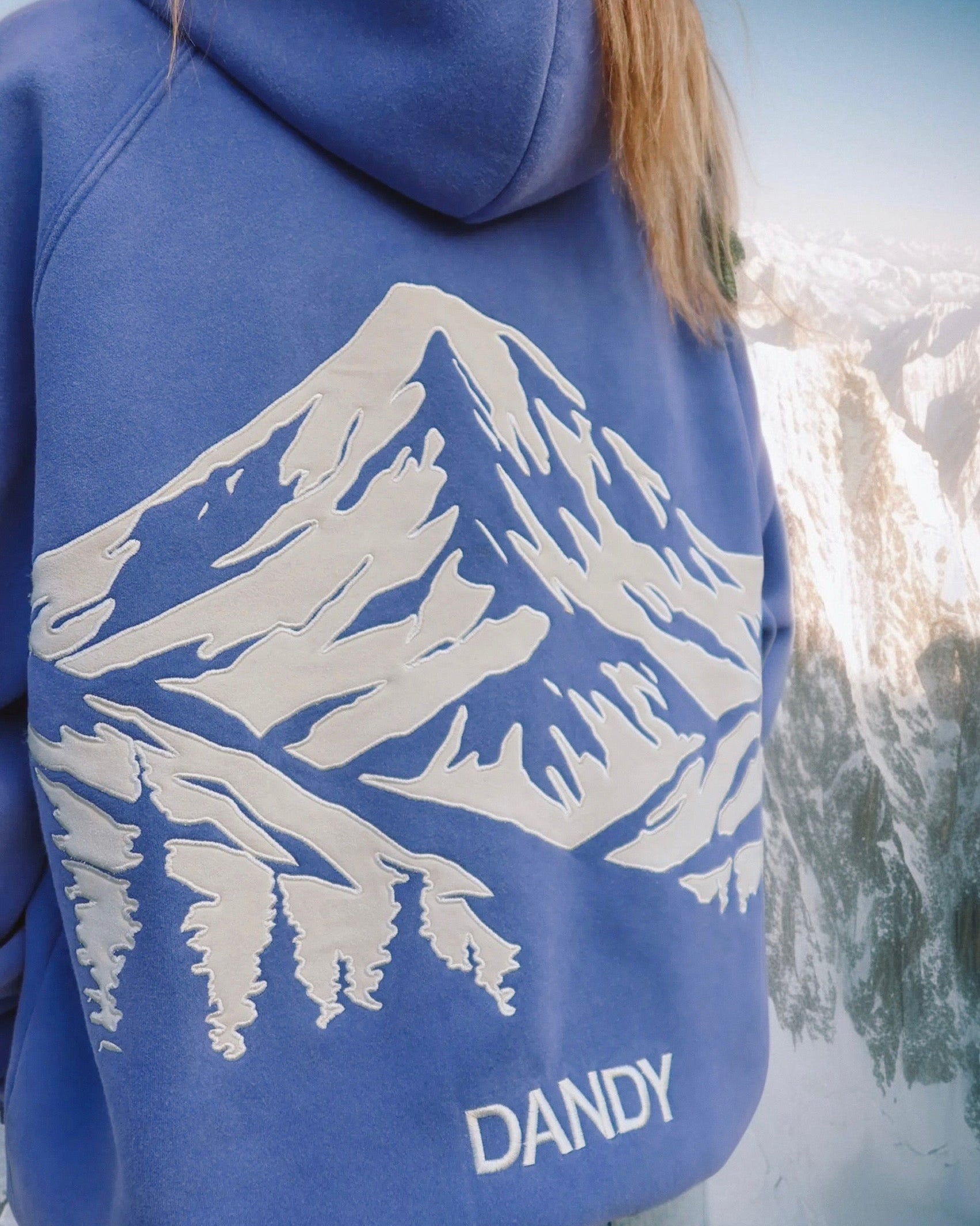 Blue hoodie with mountain design and 'DANDY' text against a mountainous background