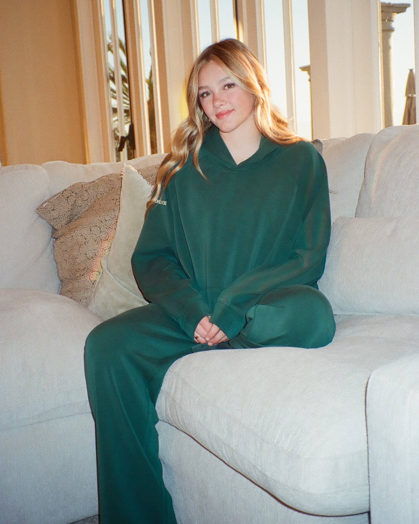 Woman wearing a green outfit sitting on a beige couch.