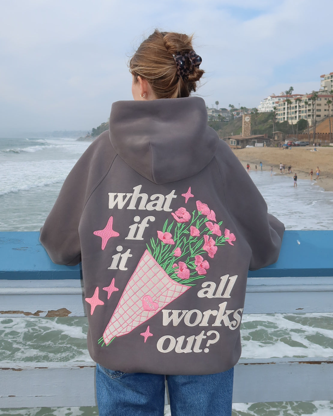 Person wearing a hoodie with a floral design and text by the beach