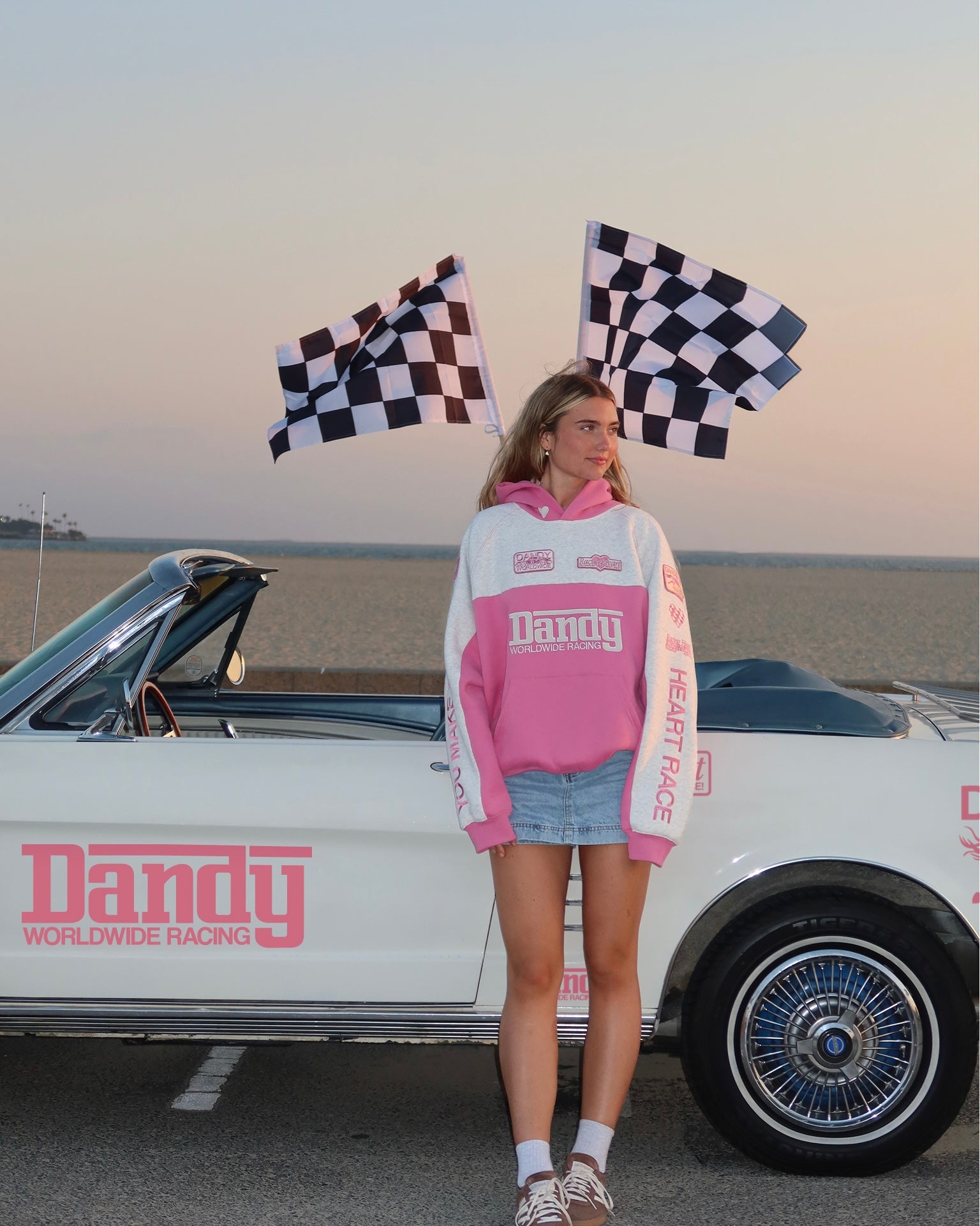 "Racing Heart" Oversized Lux Hoodie in Pink standing next to a vintage car at the beach at sunset