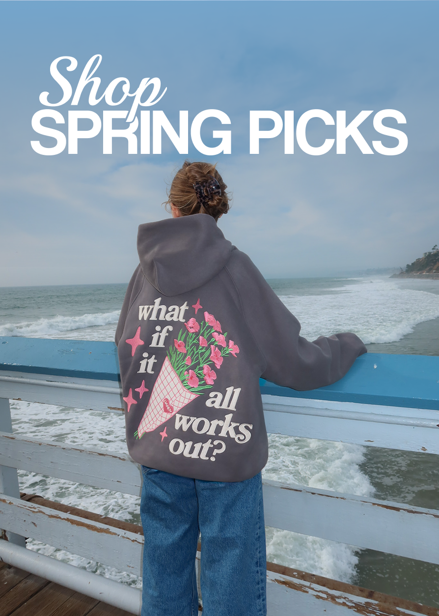 Person wearing a hoodie with a quote by the ocean, text 'Shop Spring Picks' above.