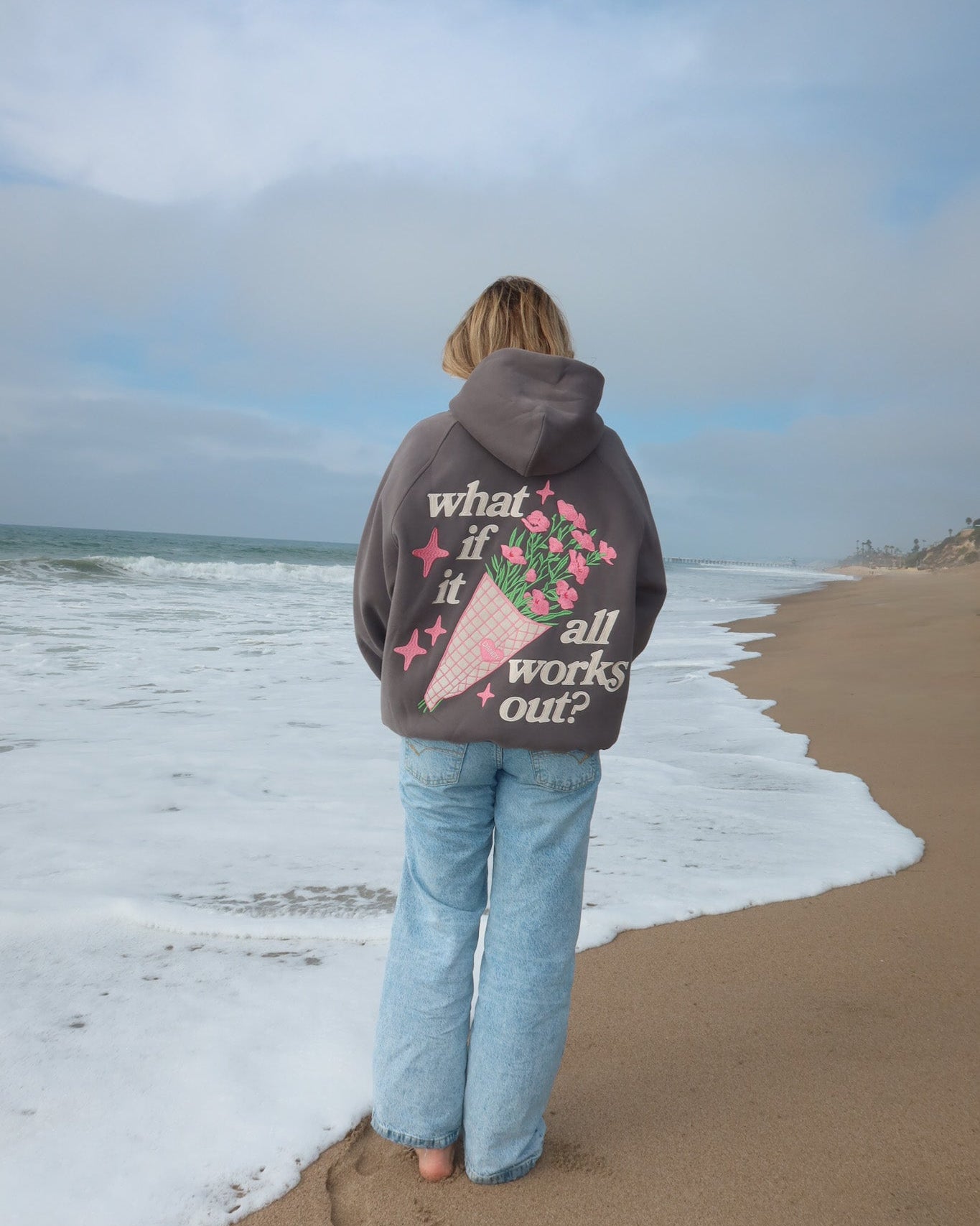 Person wearing a hoodie with a graphic and text on the beach