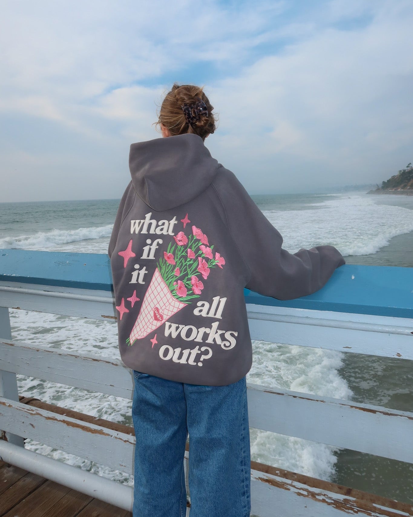 Person wearing a hoodie with a graphic design by the ocean