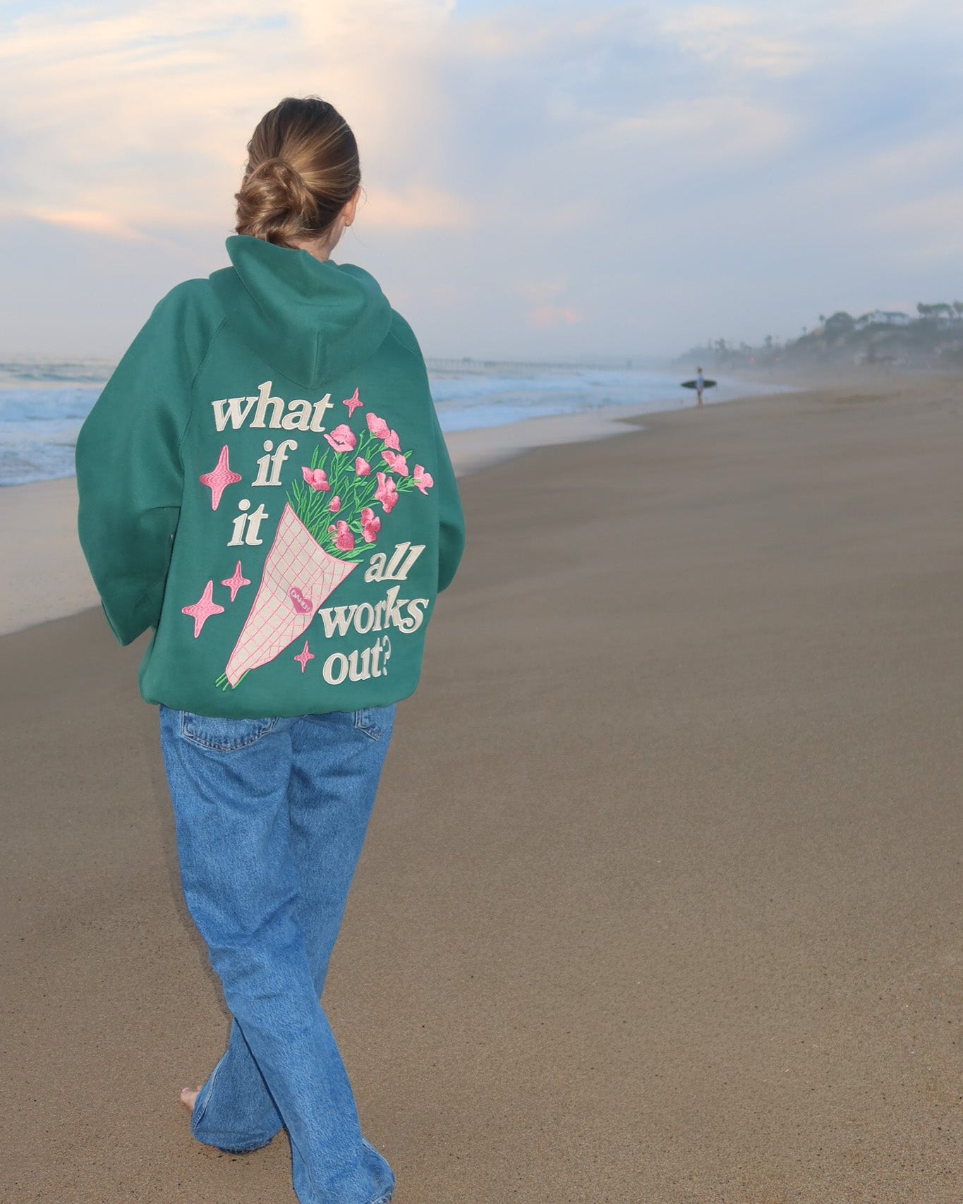 Person wearing a green sweatshirt with text and graphics on a beach