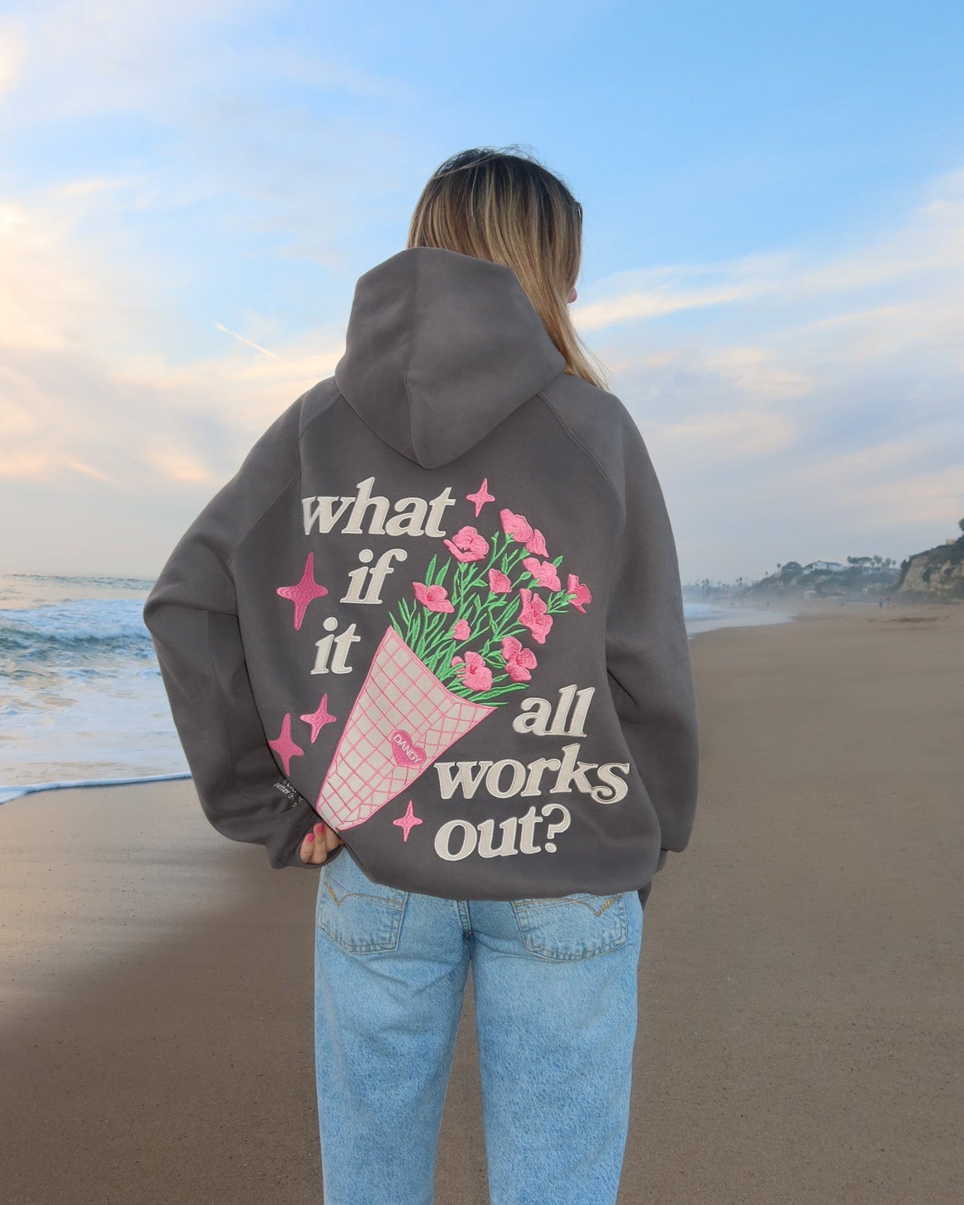 Person wearing a hoodie with a floral design and text on a beach