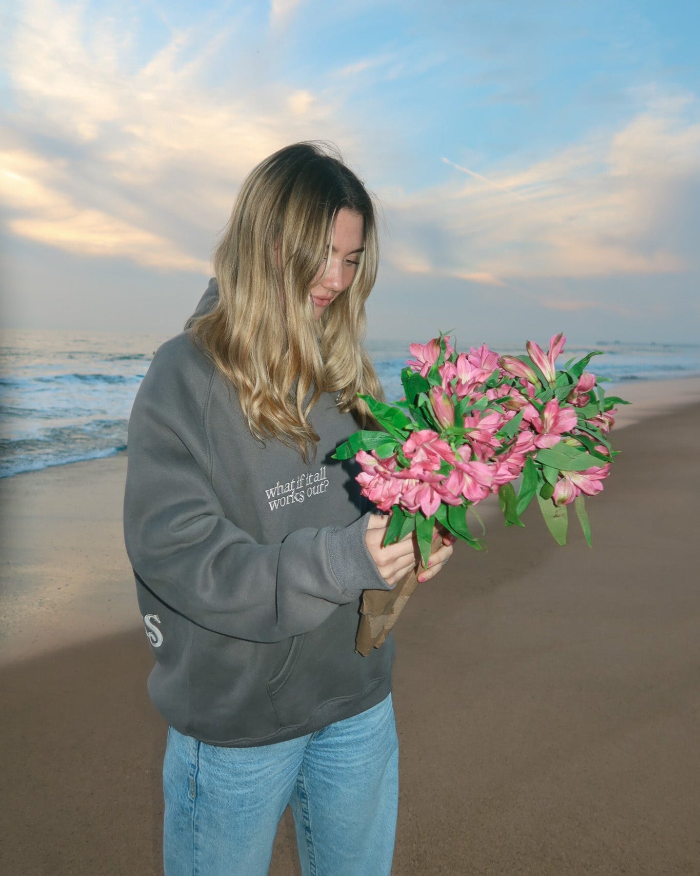 Person holding pink flowers on a beach with ocean and sky in the background