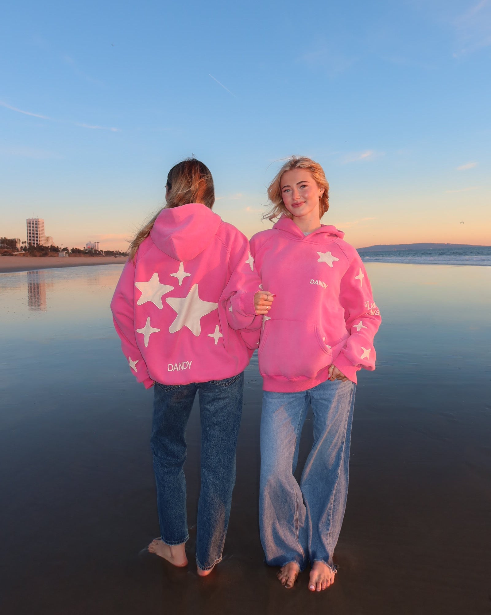Two people wearing matching pink hoodies with star patterns standing on a reflective water surface.