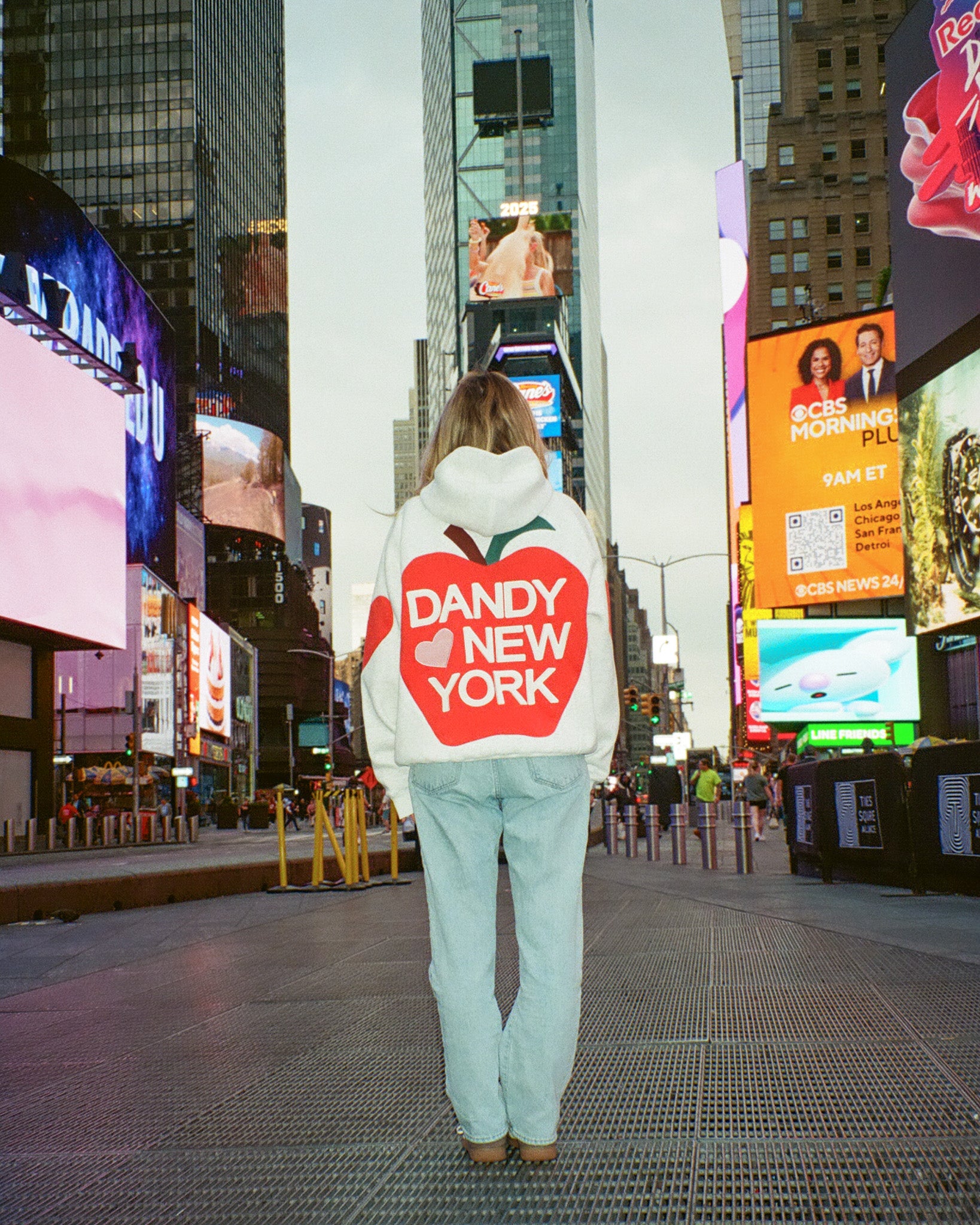 Person wearing a hoodie with 'Dandy New York' text in Times Square, New York.