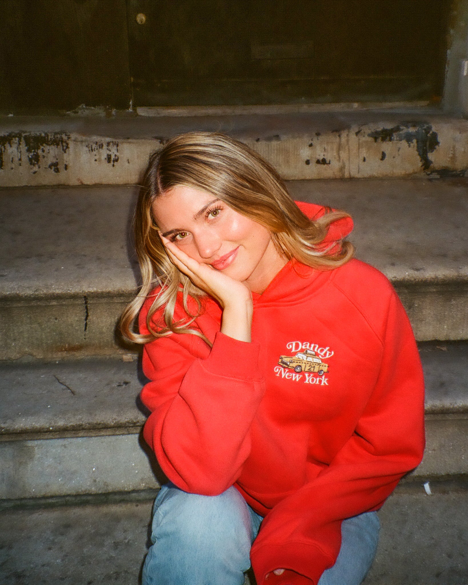 Person wearing a red hoodie with a logo sitting on steps.
