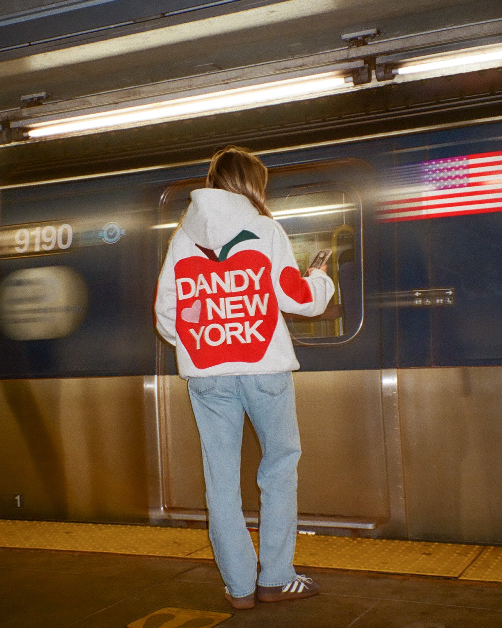 Person wearing a hoodie with 'Dandy New York' text on a subway platform