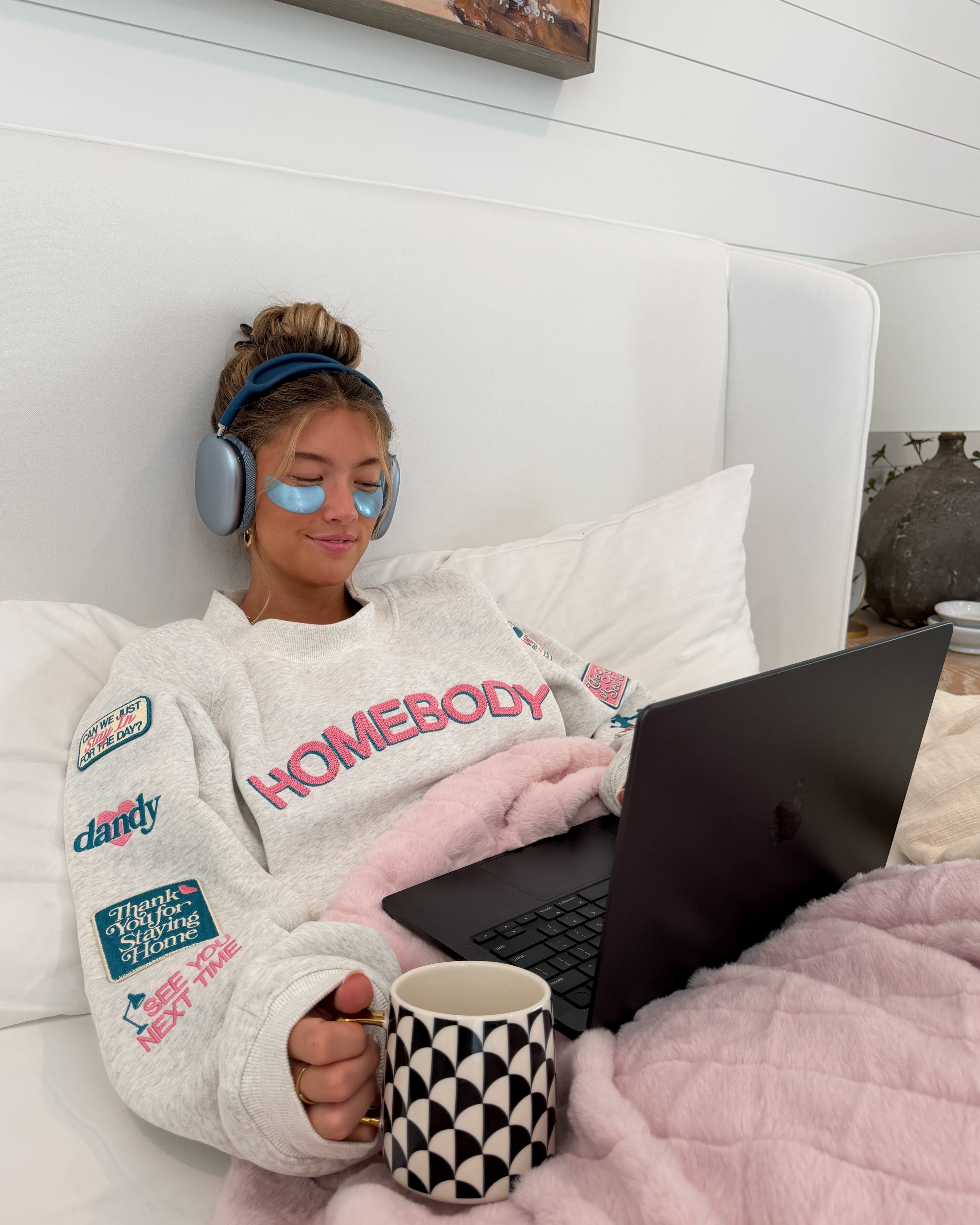 Person lying on a couch with a laptop, wearing headphones and a cozy sweater.