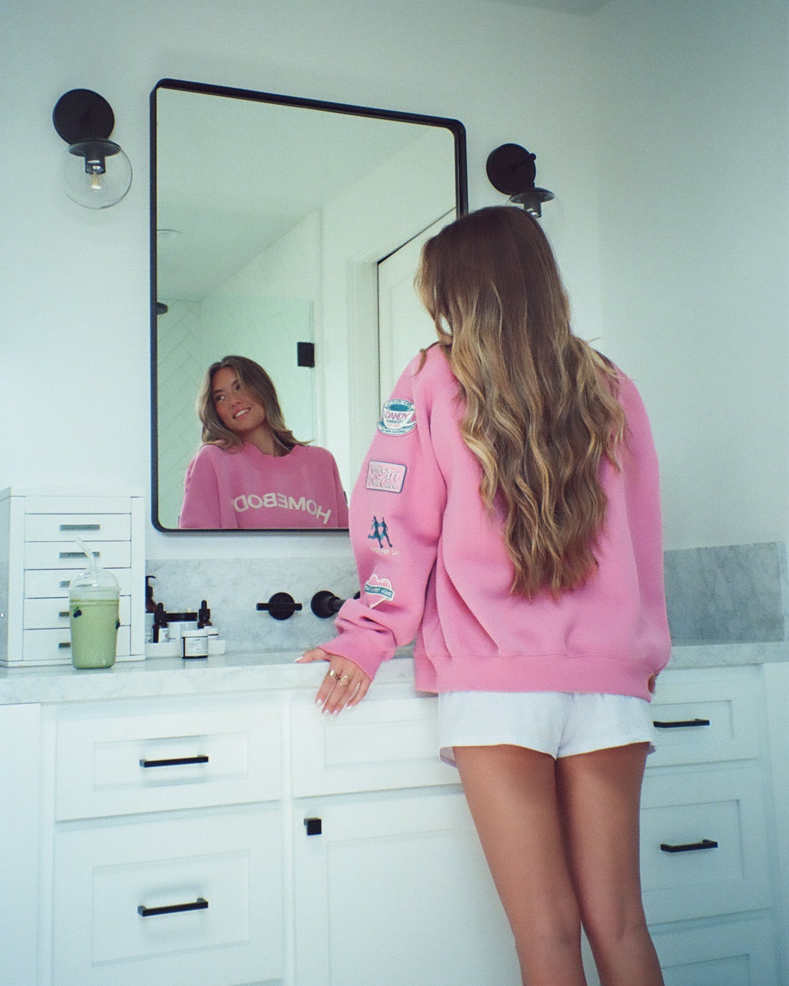 Person wearing a pink sweatshirt with visible branding in a bathroom.