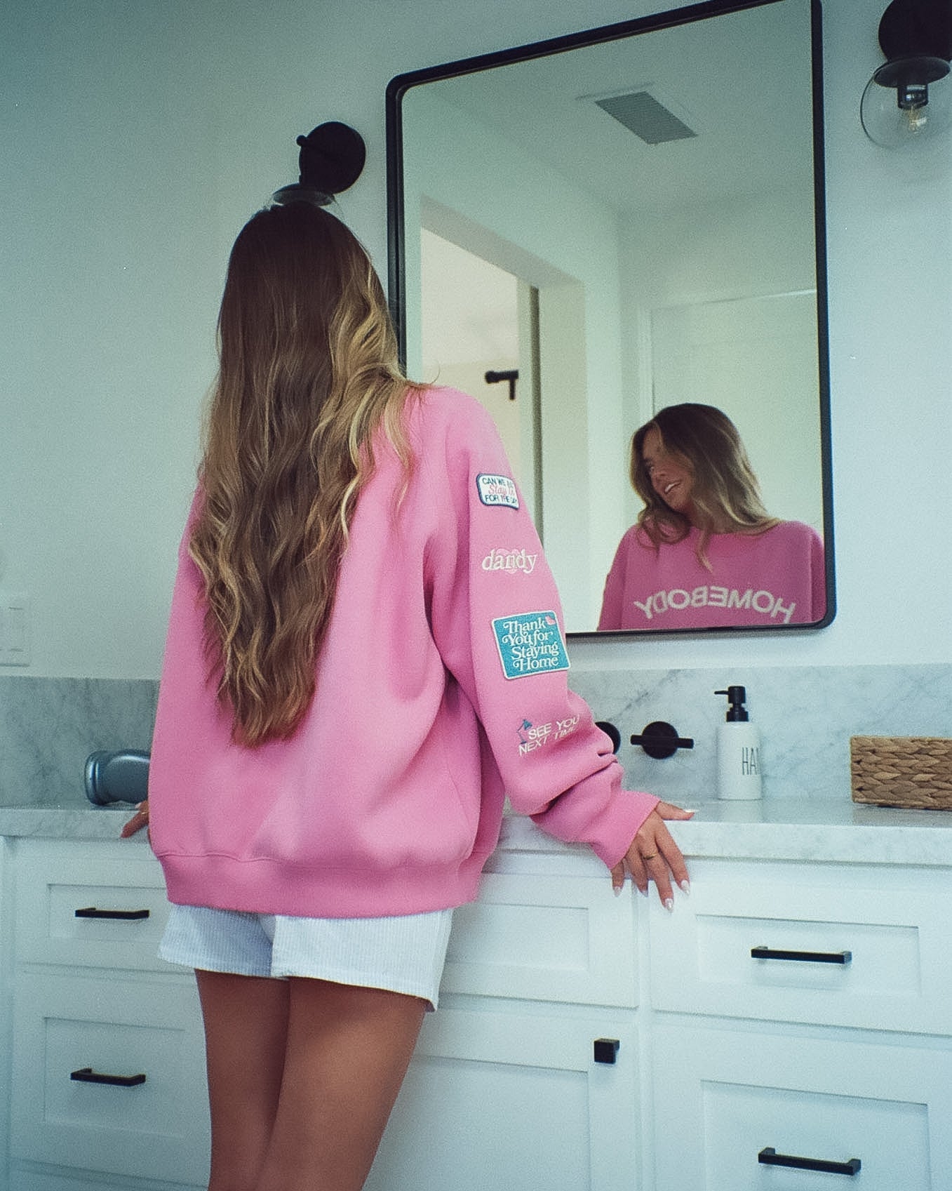 Person wearing a pink sweatshirt with a brand logo in a bathroom.
