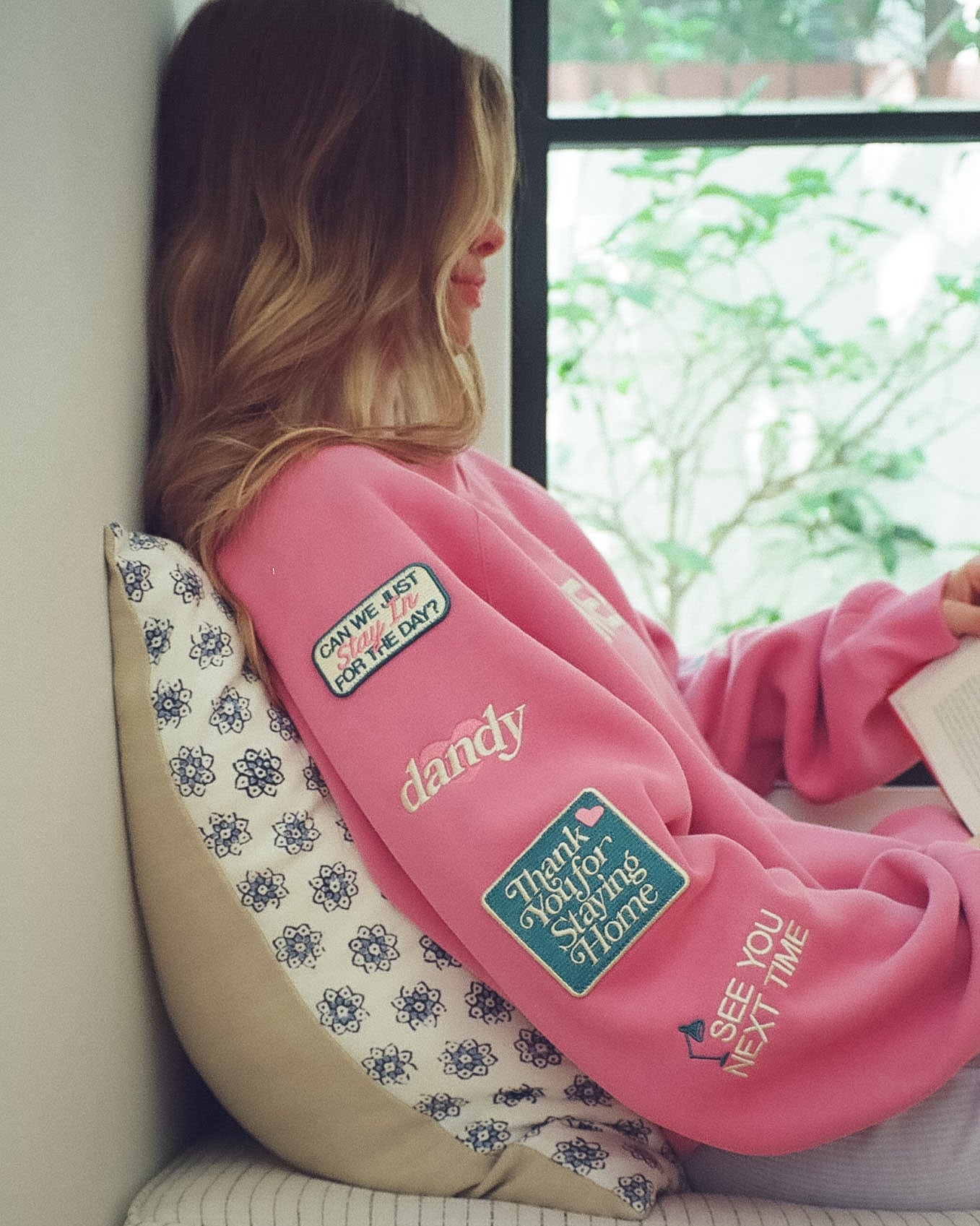 Person wearing a pink sweatshirt with various patches sitting on a couch.