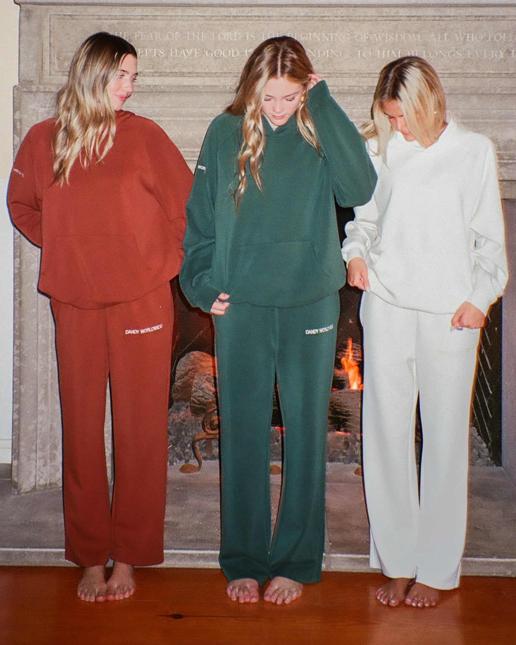 Three people wearing tracksuits in front of a fireplace.