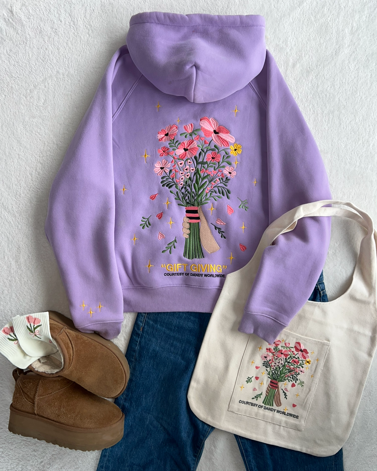 Purple hoodie with floral design, brown boots, and tote bag on a white background