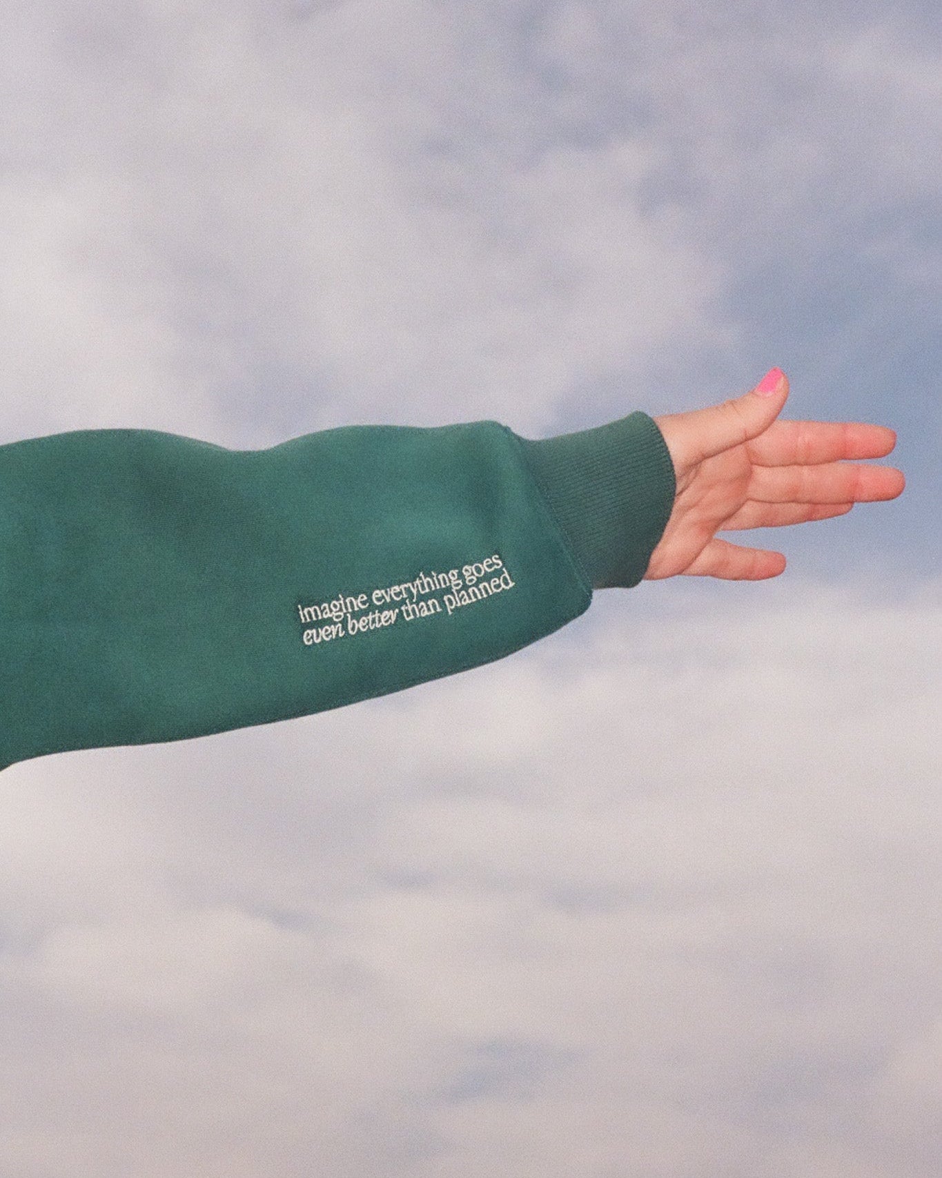 Green sweatshirt with text on sleeve against a cloudy sky