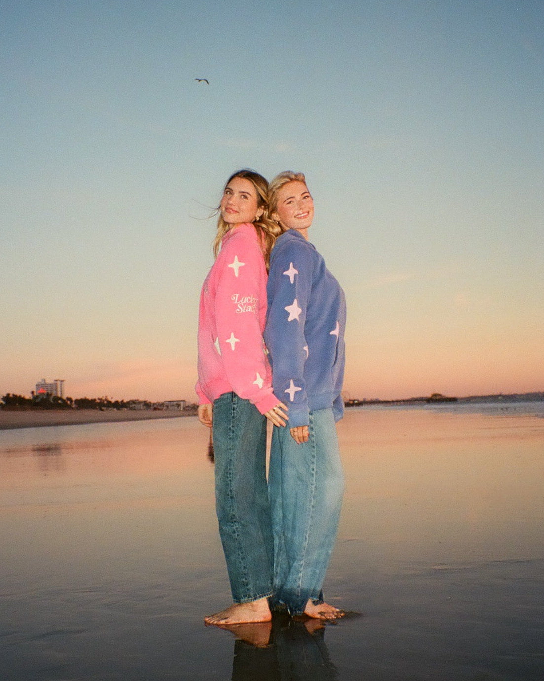 Two people standing on a beach at sunset, wearing colorful shirts with star patterns.