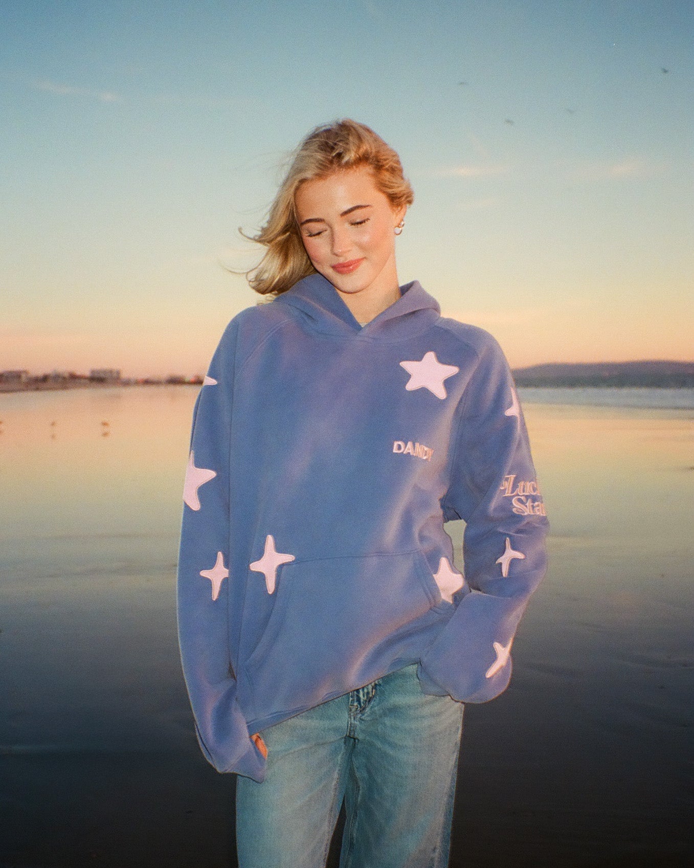 Person wearing a blue hoodie with star patterns by a body of water at sunset.