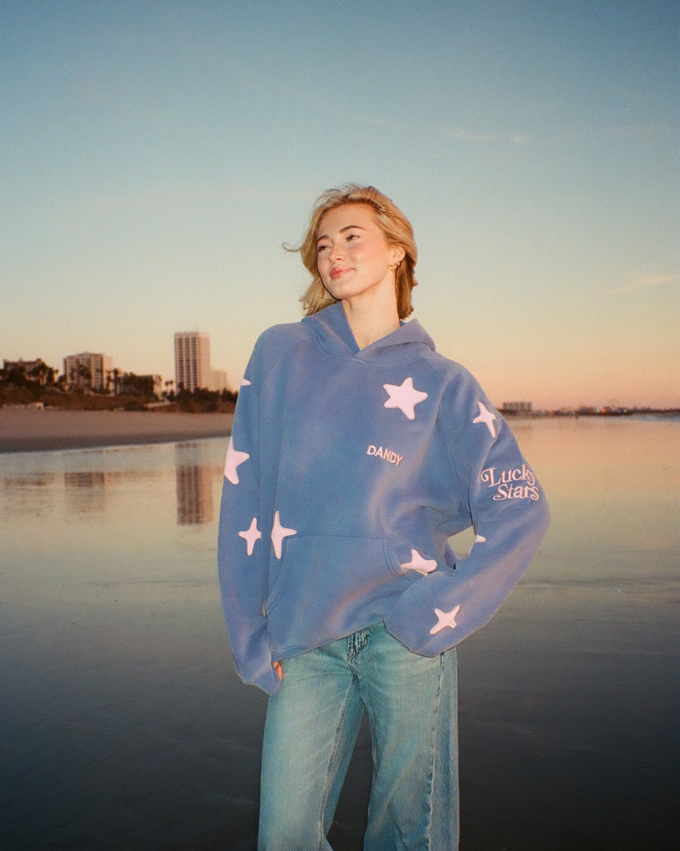 Person wearing a blue sweater with star patterns by a waterfront at sunset.