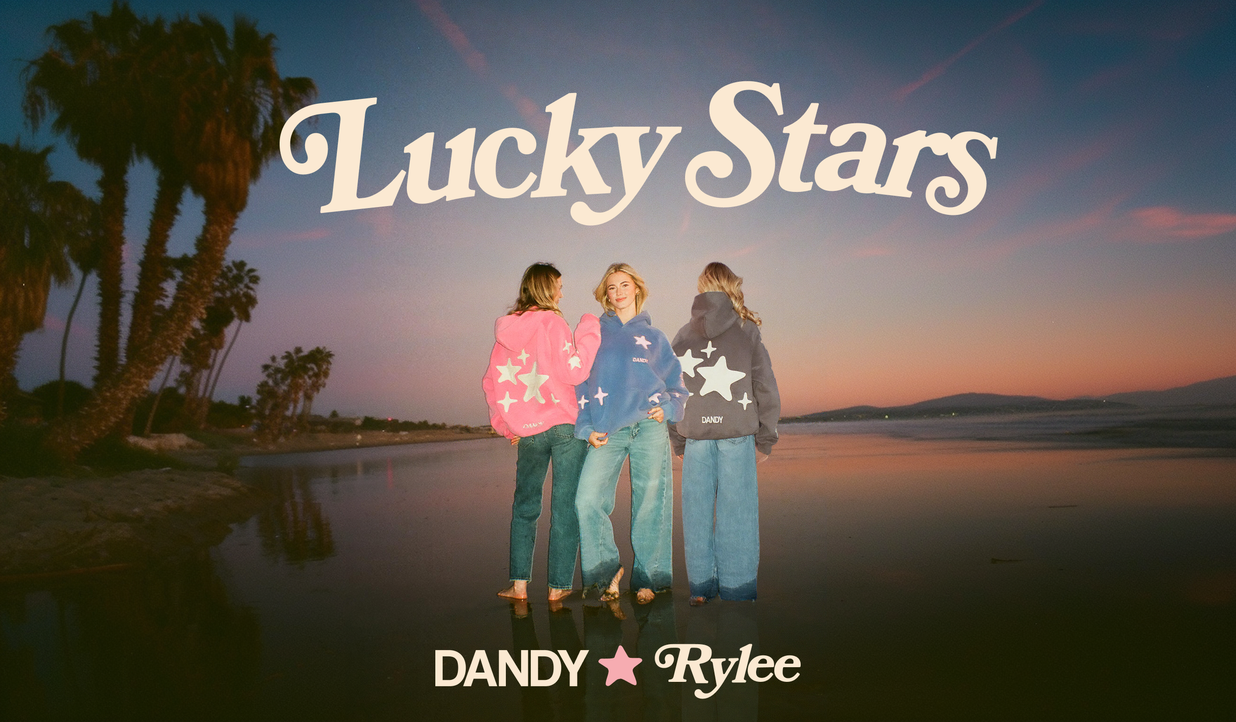 Three girls wearing star-patterned hoodies on a beach with 'Lucky Stars' text and 'Dandy Rylee' branding. 

Colors from left: Pink, Blue, Dark Gray