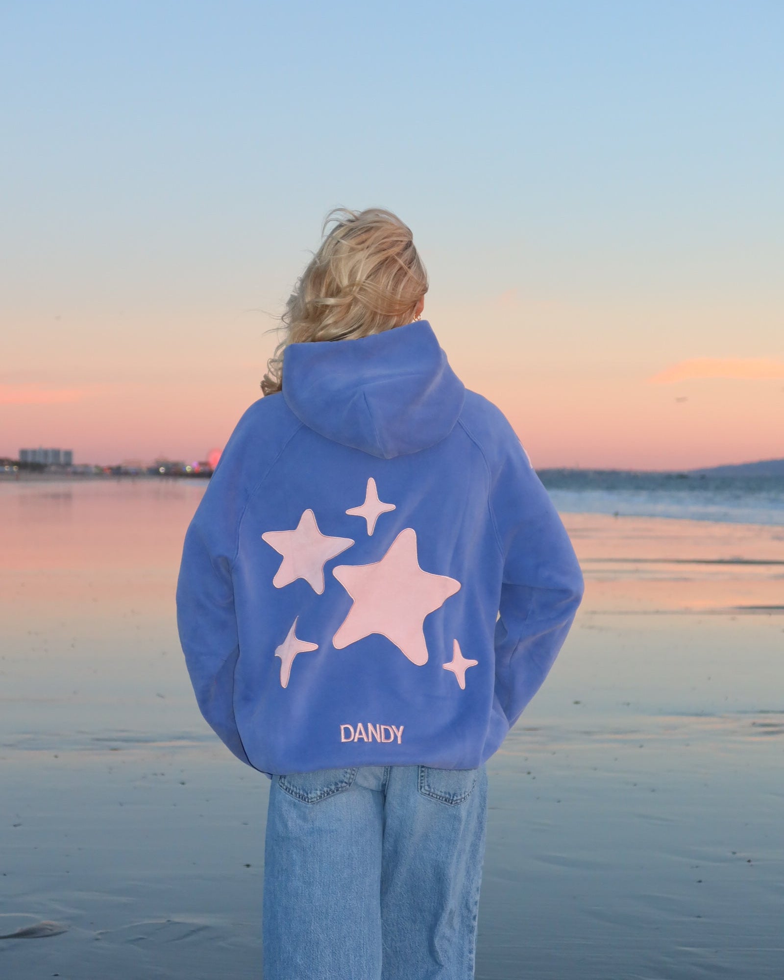 Person wearing a blue hoodie with star designs on a beach at sunset