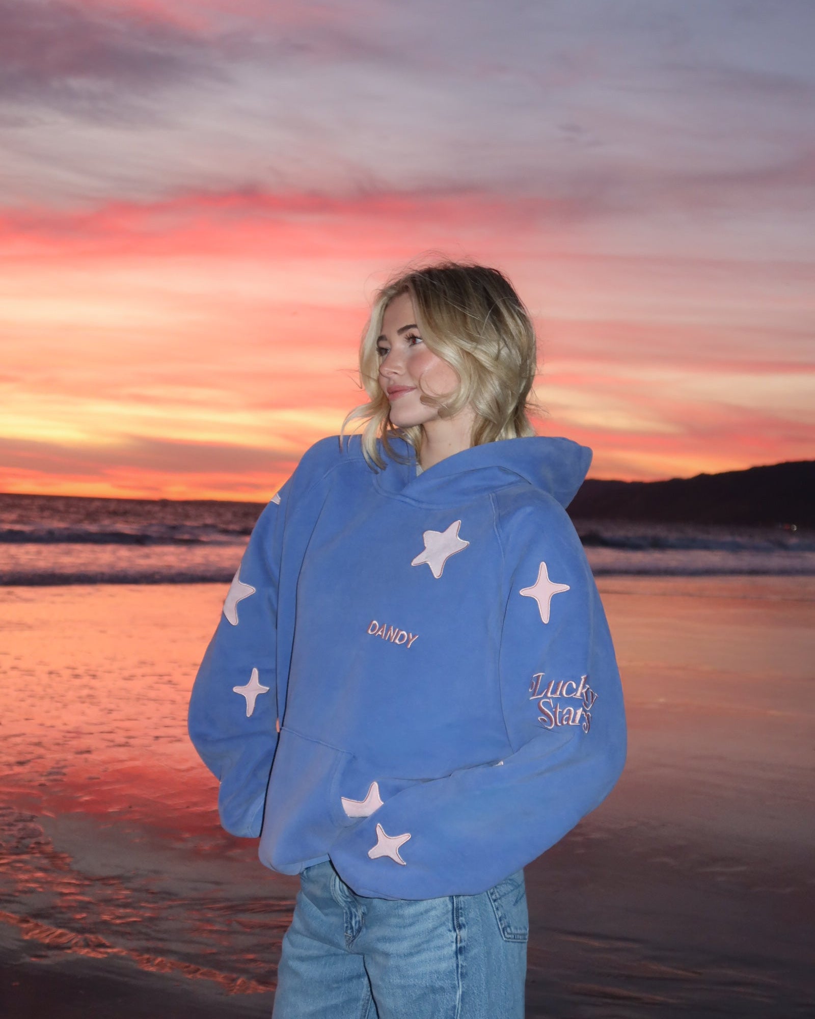 Person wearing a blue hoodie with star patterns on a beach at sunset