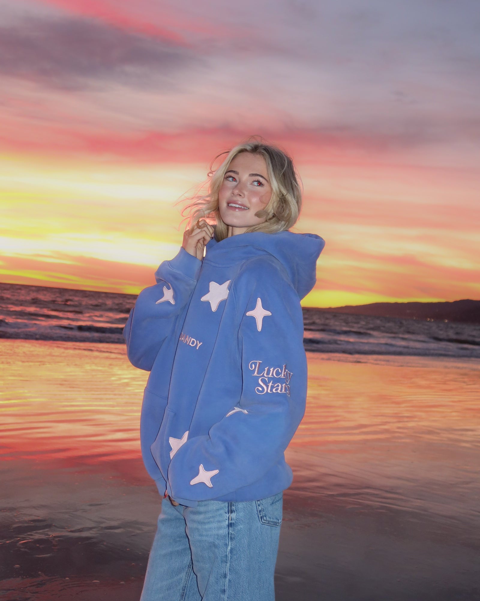 Person wearing a blue hoodie with star patterns on a beach at sunset