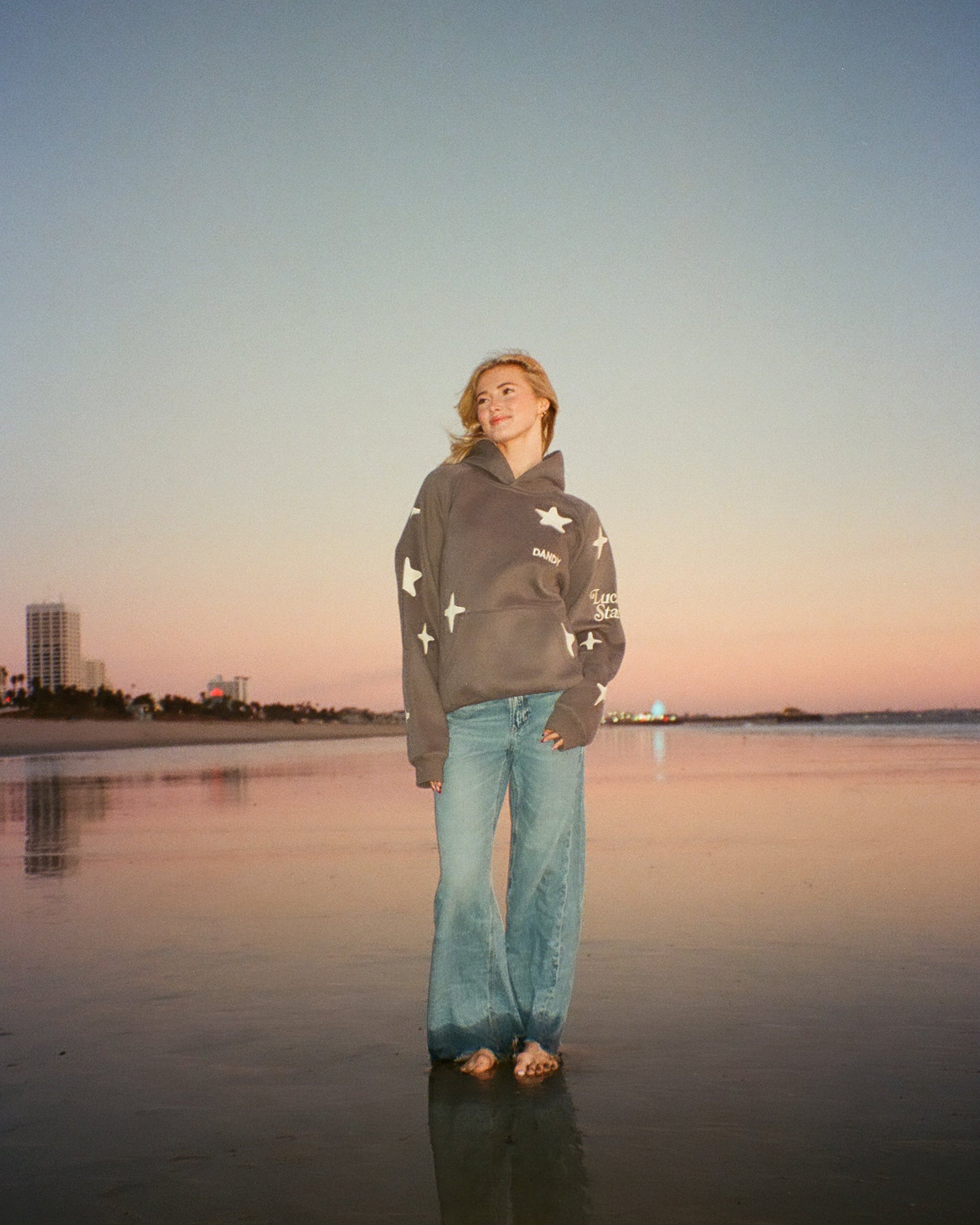 Girl wearing star hoodie and jeans. Standing in the reflective wet sand on a beach at sunset