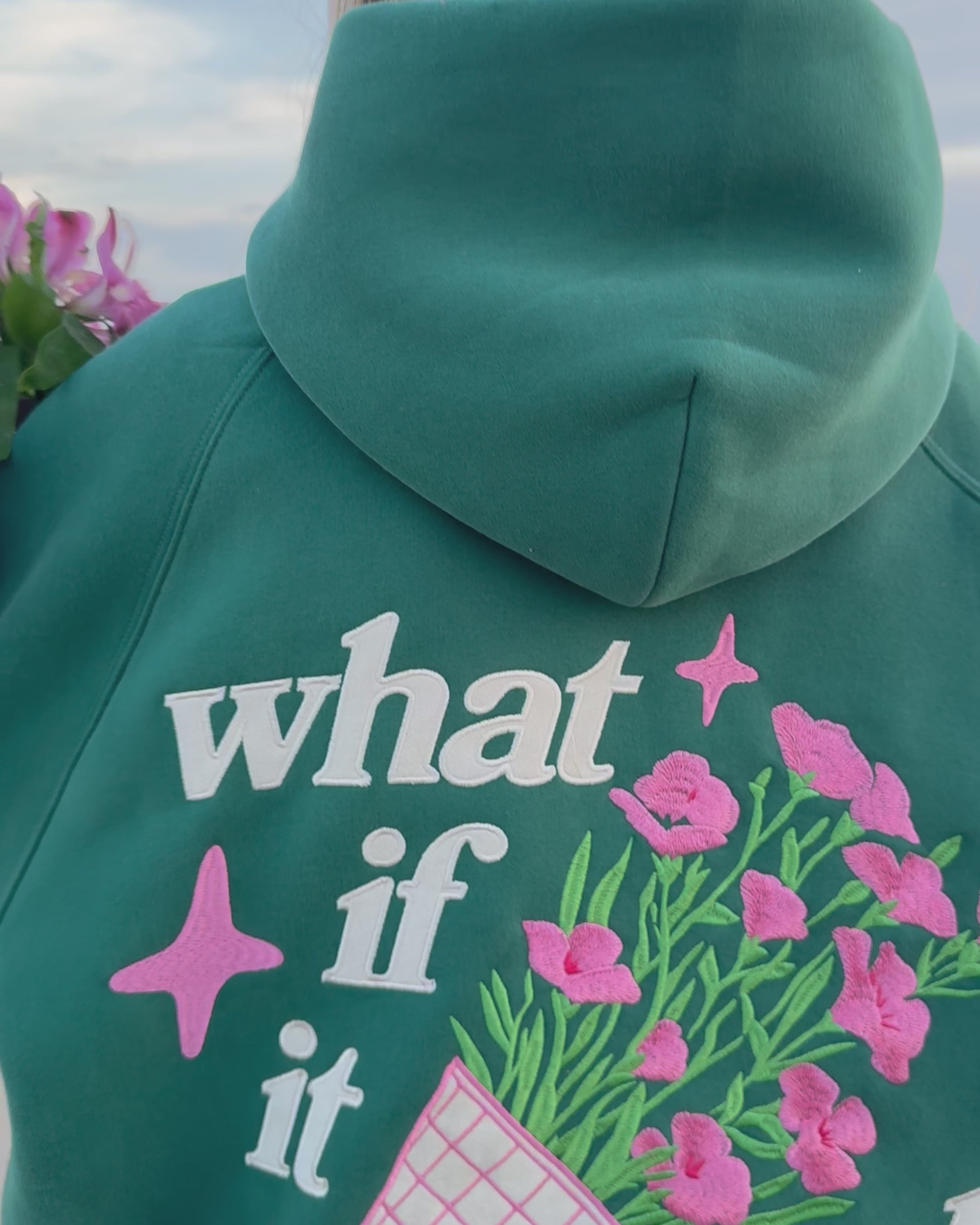 Video showing a woman walking on a sandy beach holding flowers and wearing a green hoodie
