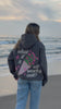 Video of a woman wearing a gray hoodie with flower embroidery on the beach at sunset